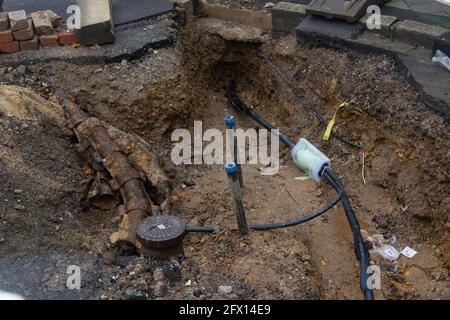 Scavato il marciapiede rivelando i fili in tubi di protezione. Costruzione di linee elettriche o cavi per telecomunicazioni, costruzione di rete ottica informaz Foto Stock