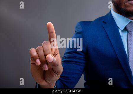 Sezione centrale dell'uomo d'affari afroamericano che tocca lo schermo invisibile contro sfondo grigio Foto Stock