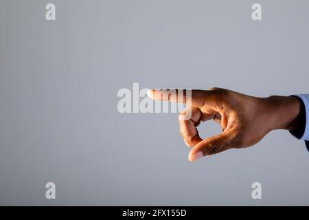 Primo piano di mano di uomo d'affari che tocca schermo invisibile contro sfondo grigio Foto Stock