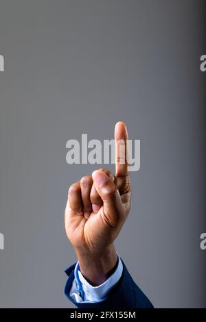 Primo piano di mano di uomo d'affari che tocca schermo invisibile contro sfondo grigio Foto Stock