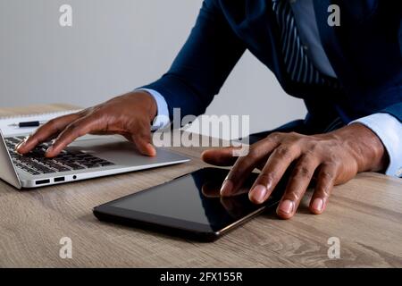 Primo piano di un uomo d'affari che utilizza un notebook e un tablet digitale sfondo grigio Foto Stock