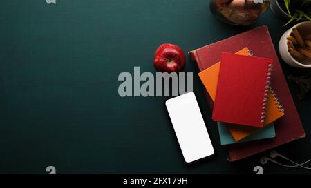 Vista dall'alto dell'area di lavoro con una pila di libri, smartphone, mela, decorazioni e spazio di copia su un tavolo verde scuro, tracciato di ritaglio Foto Stock