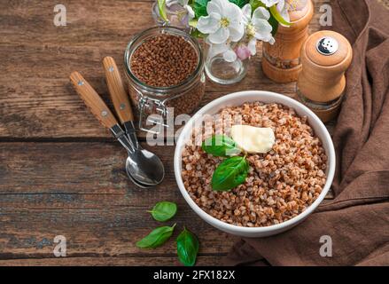 Grani di grano saraceno bolliti in una piastra bianca su uno sfondo marrone con spazio per la copia. Foto Stock