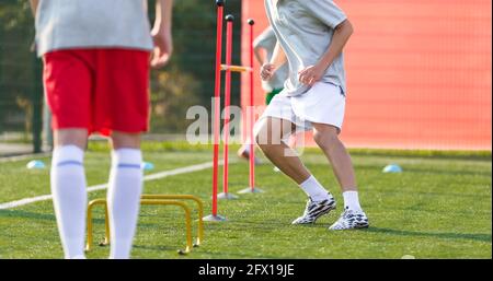 Giocatori di Teenage Football sul campo di allenamento. Young Boys Running Slalom traccia tra i poli di allenamento e saltando oltre gli ostacoli. Attrezzature da allenamento per il calcio Foto Stock