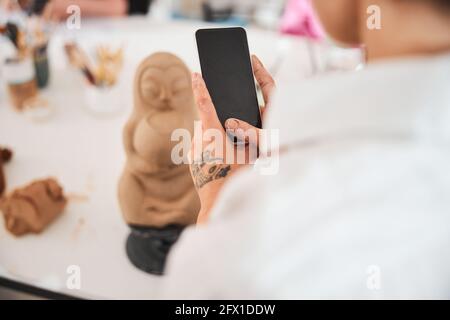Telefono cellulare nelle mani di persona vicino alla statua in ceramica Foto Stock