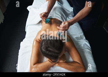 Bella giovane donna sotto l'asciugamano con massaggio professionale vetro freddo nel centro benessere Foto Stock