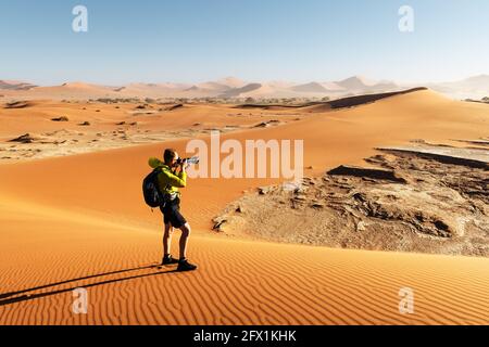 Fotografo che scatta foto a Deadvlei, Namib-Naukluft National Park, Namibia, Africa. Terreno asciutto con sabbia nel deserto del Namib durante il tramonto. Fotografia di paesaggio Foto Stock