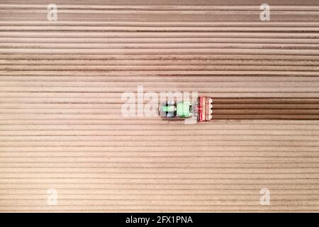 Trattore solitario su campo agricolo con file di terreno arato. Campi agricoli preparati per piantare raccolti, vista dall'alto. Concetto di agricoltura industriale. Fotografia drone Foto Stock