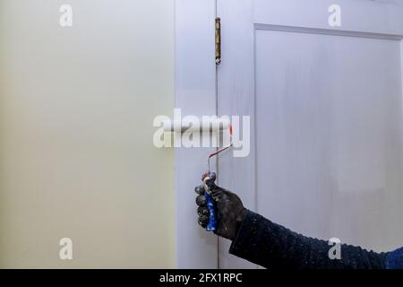 Pittore appaltatore che aggiorna i colori della verniciatura dei rivestimenti di modanatura delle porte con verniciatura a rullo manuale Foto Stock