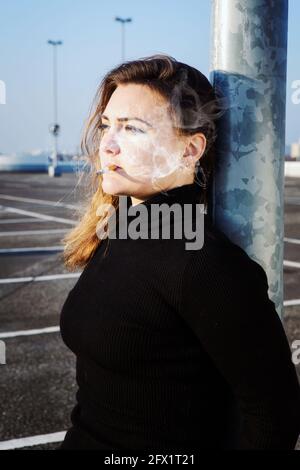 ritratto di giovane donna bruna fumando una sigaretta all'aperto a. un ponte di parcheggio Foto Stock