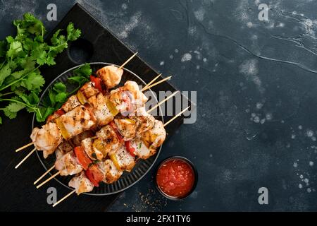 Kebab shish di pollo o kebab spiedini su tavola di legno, spezie, erbe e verdure su sfondo grigio scuro. Barbecue ingredienti crudi per goulash o. Foto Stock