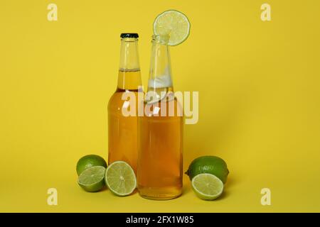 Bottiglie di birra e lime su sfondo giallo Foto Stock