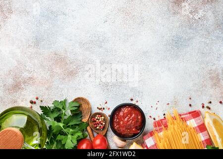 Pasta di fondo. Spaghetti di pasta, salsa di ketchup di pomodoro, olio d'oliva, spezie, prezzemolo, e pomodori freschi su un tavolo di ardesia grigio chiaro. Cucina alimentare Foto Stock