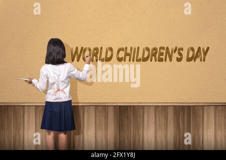 Vista posteriore di Asian cute girl pittura un mondo bambini giorno testo sulla parete. Giornata mondiale dei bambini Foto Stock