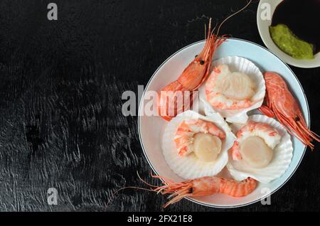 Capesante grezzo naturale con gamberi bolliti nel lavandino in una ciotola di ceramica con salsa di soia e wasabi su fondo scuro. Messa a fuoco selettiva. Foto Stock