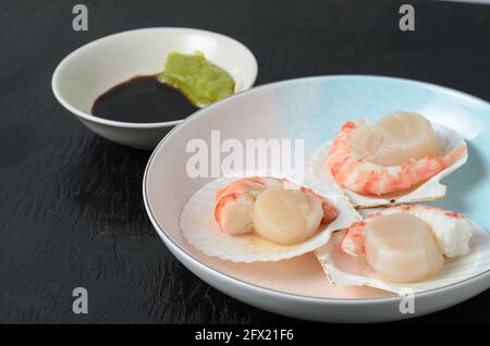 Capesante grezzo naturale con gamberi bolliti nel lavandino in una ciotola di ceramica con salsa di soia e wasabi su fondo scuro. Messa a fuoco selettiva. Foto Stock