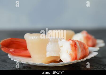 Capesante crudo con coda di gamberi bollita in conchiglia su una superficie di legno nero. Messa a fuoco selettiva. Foto Stock