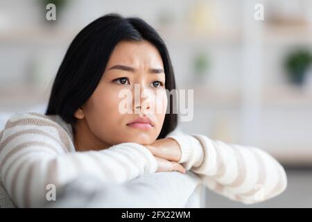 Concetto di depressione. Closeup di sconvolto Asian Female seduta sul divano a casa Foto Stock