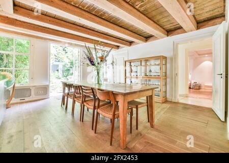 Tavolo da pranzo in legno con sedie sotto il soffitto con travi in legno in accogliente camera di campagna di casa Foto Stock