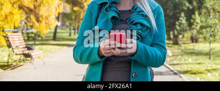 Foto di primo piano delle mani femminili con smartphone. Via d'autunno sullo sfondo Foto Stock