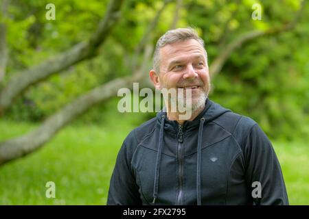 Uomo sorridente felice mentre gode un giorno nel parcheggia in primavera guardando qualcosa fuori dalla cornice un'espressione interessata Foto Stock