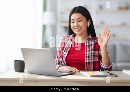 Riunione online. Donna asiatica sorridente che effettua videochiamate sul laptop a casa Foto Stock