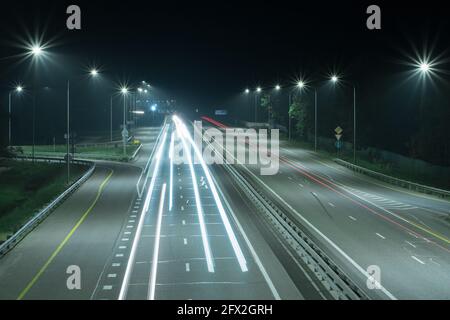 Strada notturna con lunghe strisce luminose rosse e bianche dai fari delle auto. Ci sono semafori ai bordi della strada. Scene notturne Foto Stock