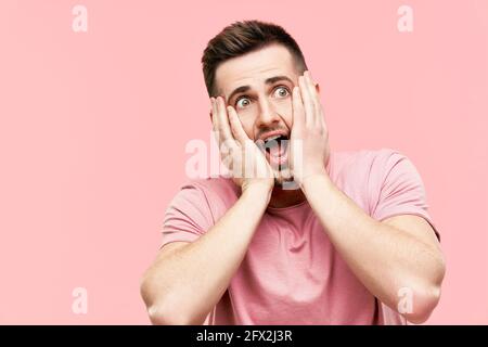 Primo piano ritratto di un uomo scosso emozionato con bocca aperta che si apre su sfondo rosa. Espressione del volto, omg, concetto di emozioni. Foto Stock