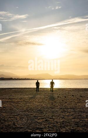 Due uomini che camminano verso l'acqua di mare. Al tramonto. Camminano a parte. Foto Stock