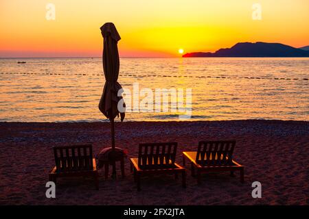 Chaise lounges e ombrellone sulla spiaggia al crepuscolo. Fantastica vacanza estiva costiera. Spiaggia sull'isola di sera. Tramonto sul se Foto Stock