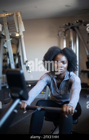 Donna giovane in forma nera che lavora su vogatore, una persona, modello capelli naturali, afroamericano, vogatore, sfondo sportswear, primo piano Foto Stock