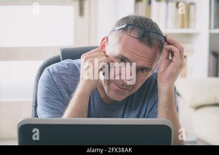 Stanchi e affaticati freelancer tenendo la sua testa in mano mentre è seduto al suo posto di lavoro in ufficio o a casa Foto Stock