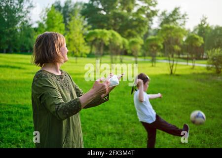 La donna felice toglie la maschera di faccia, il figlio del ragazzo gioca la sfera sull'erba Foto Stock