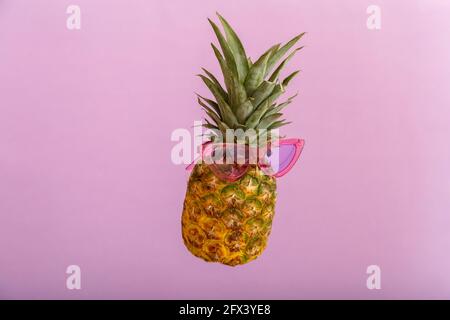 Ananas facce creative in occhiali da sole a colori su sfondo estivo di colore rosa. Tropicale frutta di ananas estate levitating in vetri rosa del sole. Estate Foto Stock
