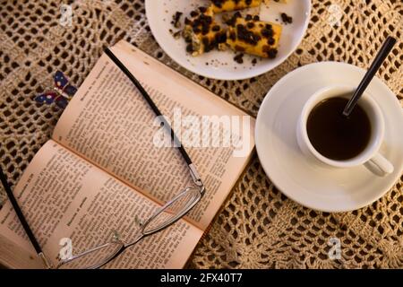 Posa piatta di un tavolo con un tradizionale uncinetto, su cui c'è una bibbia aperta con bicchieri da lettura in cima e alcune picche accanto ad un caffè Foto Stock