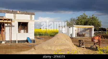 Casa rurale in costruzione con campo di colza e nubi tempestose in background. Foto Stock