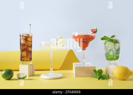 Freschezza cocktail diversi mojito, cuba libre, cocktail margarita con lime, fragole e limone su sfondo giallo moderno. Freschezza estiva Foto Stock