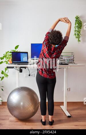 Donna che telelavoro su una scrivania regolabile in piedi accanto a a. montare la sfera Foto Stock