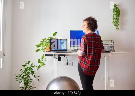 Donna che telelavoro su una scrivania regolabile in piedi accanto a a. montare la sfera Foto Stock