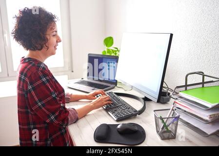 Donna che scrive sul computer su una scrivania regolabile, in una giornata di lavoro da casa Foto Stock
