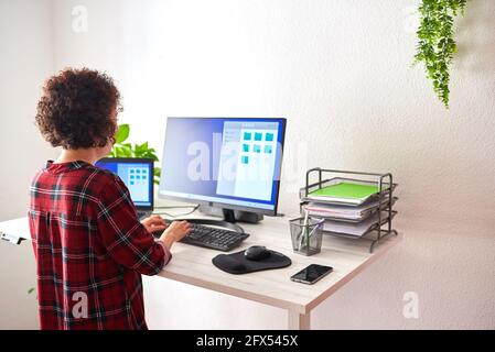 Donna che scrive sul computer su una scrivania regolabile, in una giornata di lavoro da casa Foto Stock