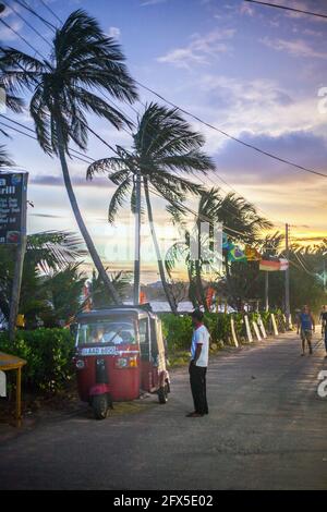 Auto Rickshaw in attesa sul lato della strada con palme e cielo viola al tramonto, Tangalle, Provincia del Sud, Sri Lanka Foto Stock