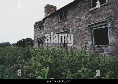 Una casa misteriosa, abbandonata, rovinata. Con serramenti vuoti e ingresso bloccato da piante. Foto Stock