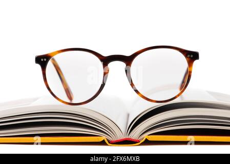 Primo piano di un libro aperto con occhiali da lettura isolati su sfondo bianco, vista frontale Foto Stock
