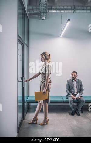 Donna che entra in ufficio uomo seduto in corridoio Foto Stock