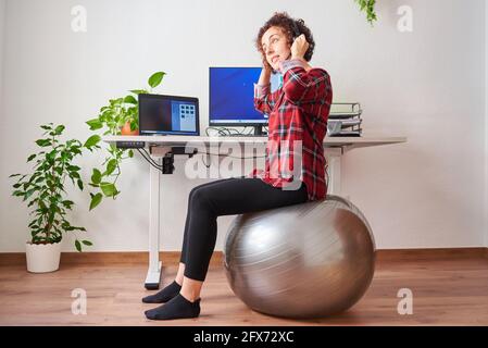 Donna che lavora in telelavoro seduto su un flipper di fronte a lei parlare in scrivania con un auricolare Foto Stock