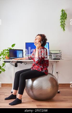 Donna che lavora in telelavoro seduto su un flipper di fronte a lei parlare in scrivania con un auricolare Foto Stock