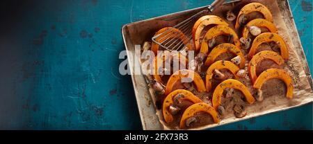 Dall'alto di appetitosa zucca affettata arrostita con champignons e. spezie aromatiche in teglia da forno su tavola blu Foto Stock