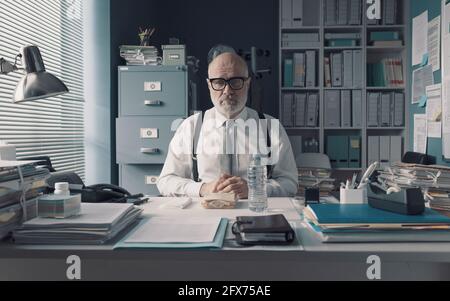 Uomo d'affari che ha un triste pranzo al tavolo da solo nel ufficio Foto Stock