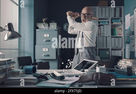 Crazy ha sottolineato uomo d'affari distruggendo la sua scrivania e laptop con una mazza da baseball, lavoro burnout concetto Foto Stock